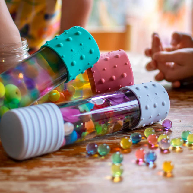 Colorful beaded tubes on a wooden surface with children's hands in the background