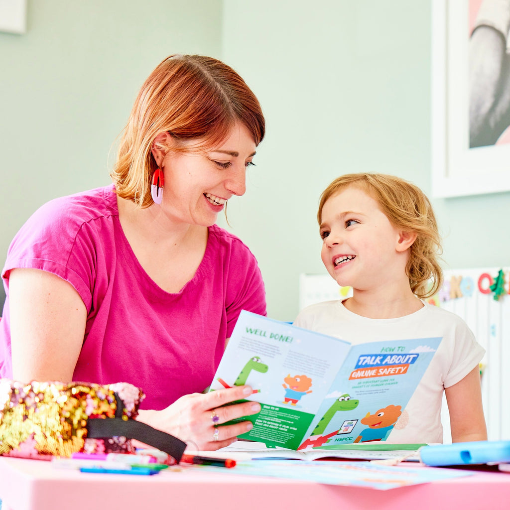 A woman and child reading the Techosaurus Activity Pack together sitting at a table and smiling. 