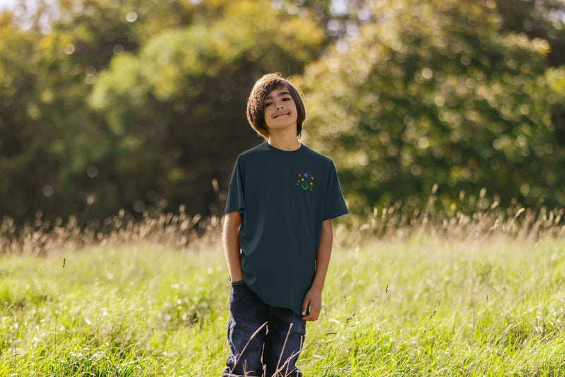 A child standing in a field, wearing a dark blue t-shirt with a colourful flower design.