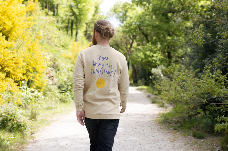 A man walking on a path, wearing a cream sweatshirt that says 